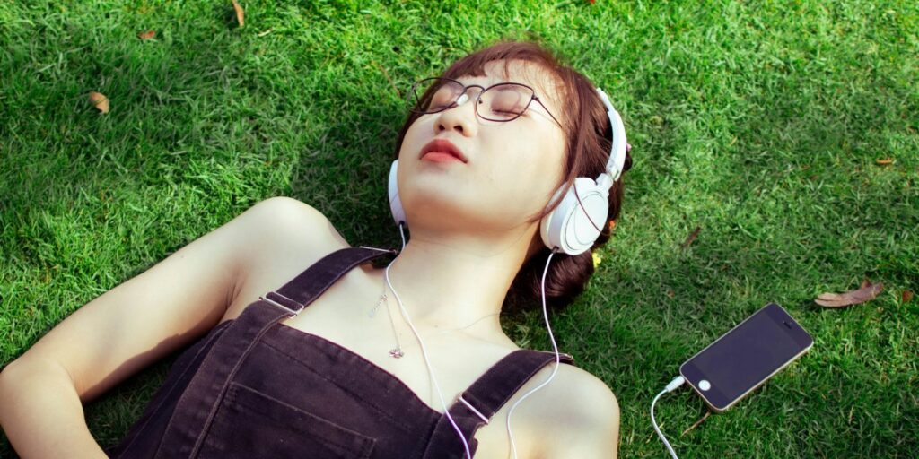 芝生に寝そべり、ヘッドホンとスマートフォンで音楽を聴く人