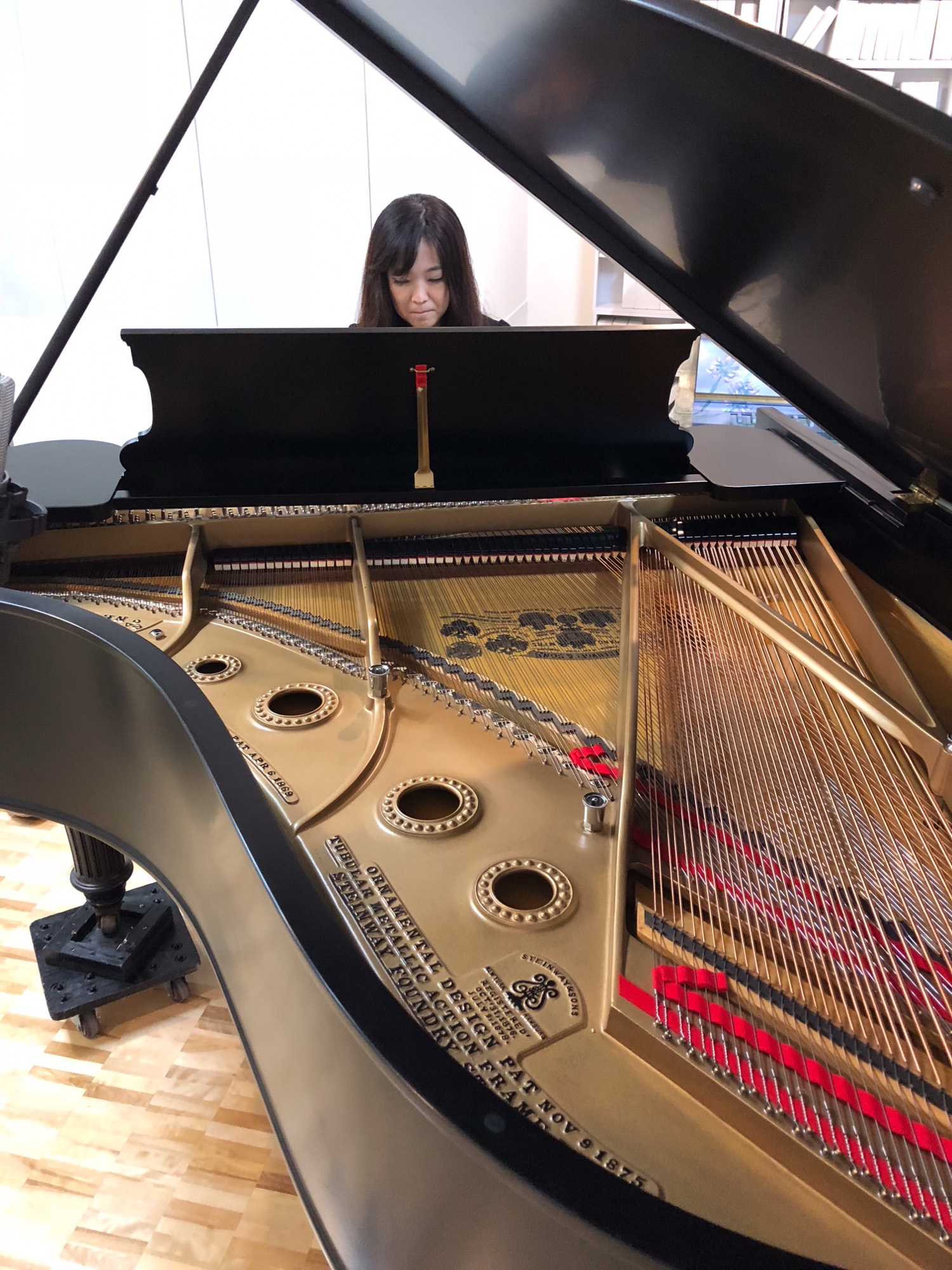 グランドピアノの弦とフレーム越しに見た、試打室で演奏する草野由花子さん