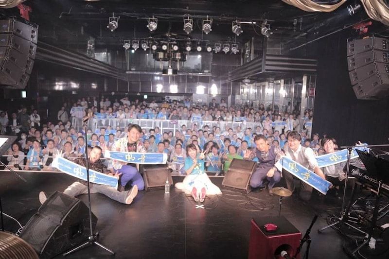 終演後、ステージ上の佐藤実絵子とバンドメンバー、客席の観客がタオルを掲げて記念撮影